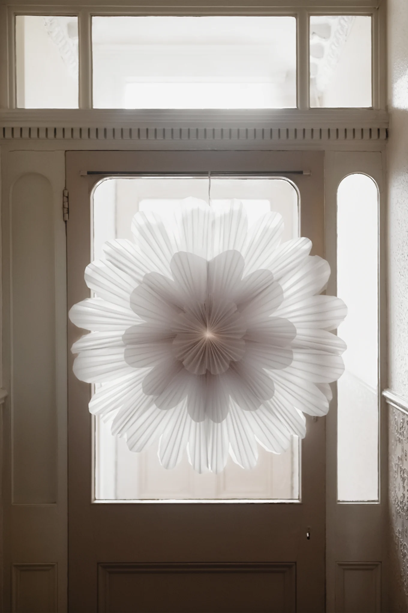 Minimalist Christmas decor - here you see the Snöblomma paper Christmas star hanging in a door way with light shining through from behind.