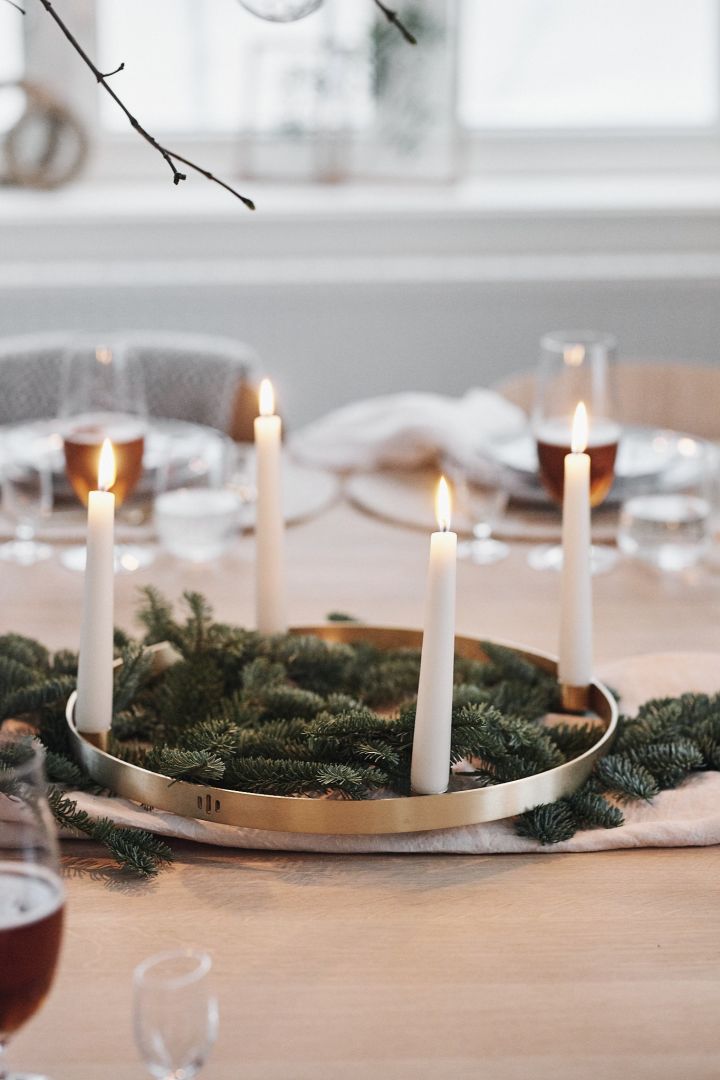 Spruce branches and a round brass candle holder with white candles stand in the middle of a white Christmas table and create a festive mood.