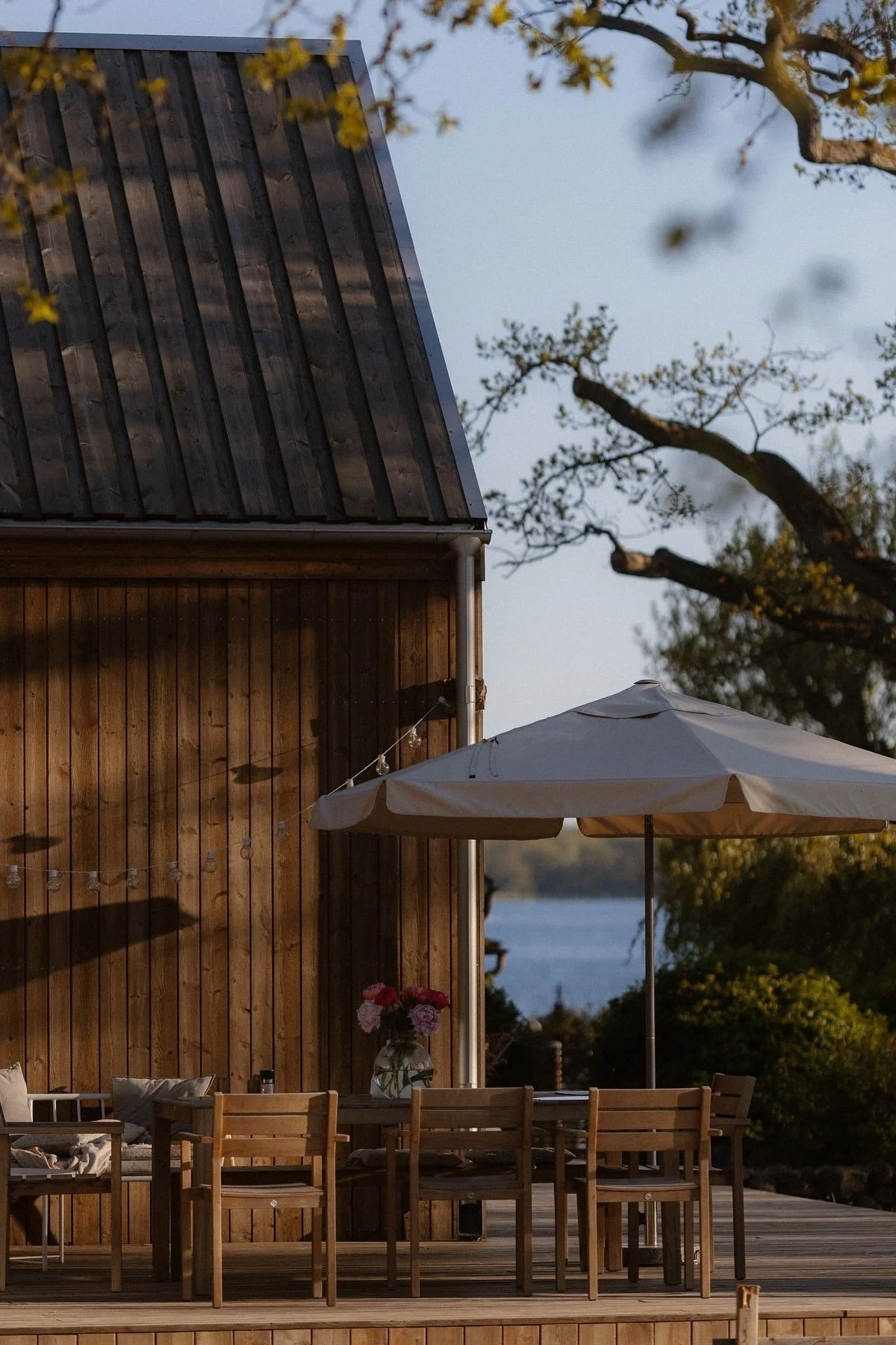 A cosy patio in front of a wooden house with a dining area with Sköndal chairs from 1898 and a parasol.