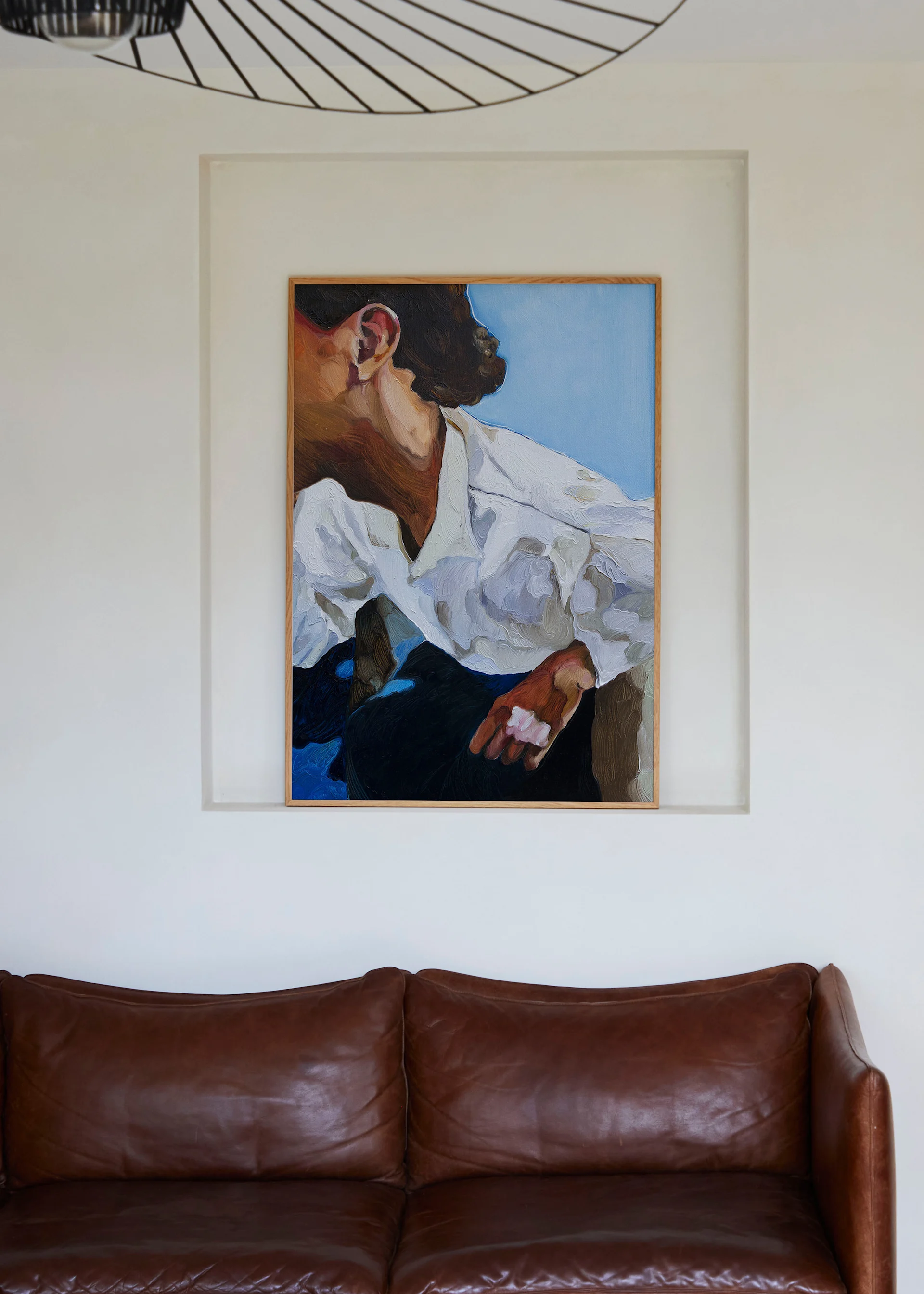 A vibrant painting of a person's profile in a white shirt, set in a wall niche, hangs above a textured brown leather sofa.