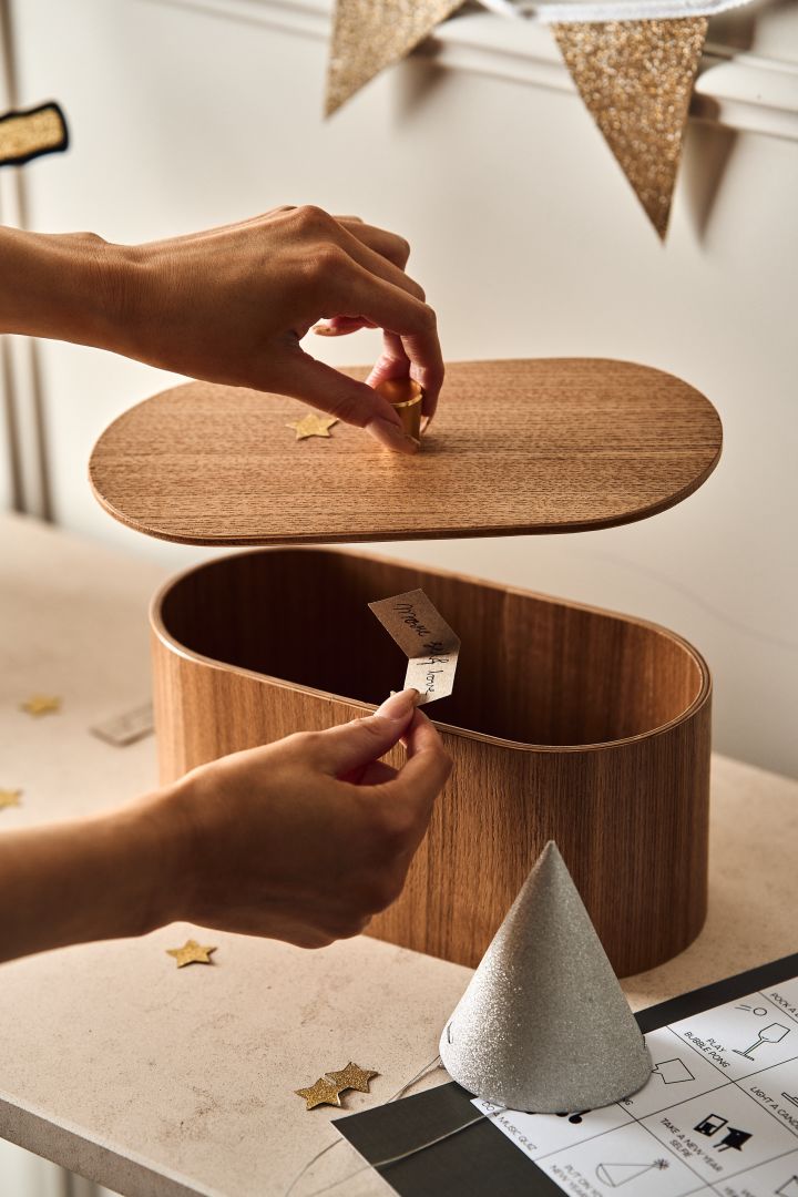 New year party ideas - here you see a hand putting a new years resolution into a wooden box from HK living. 