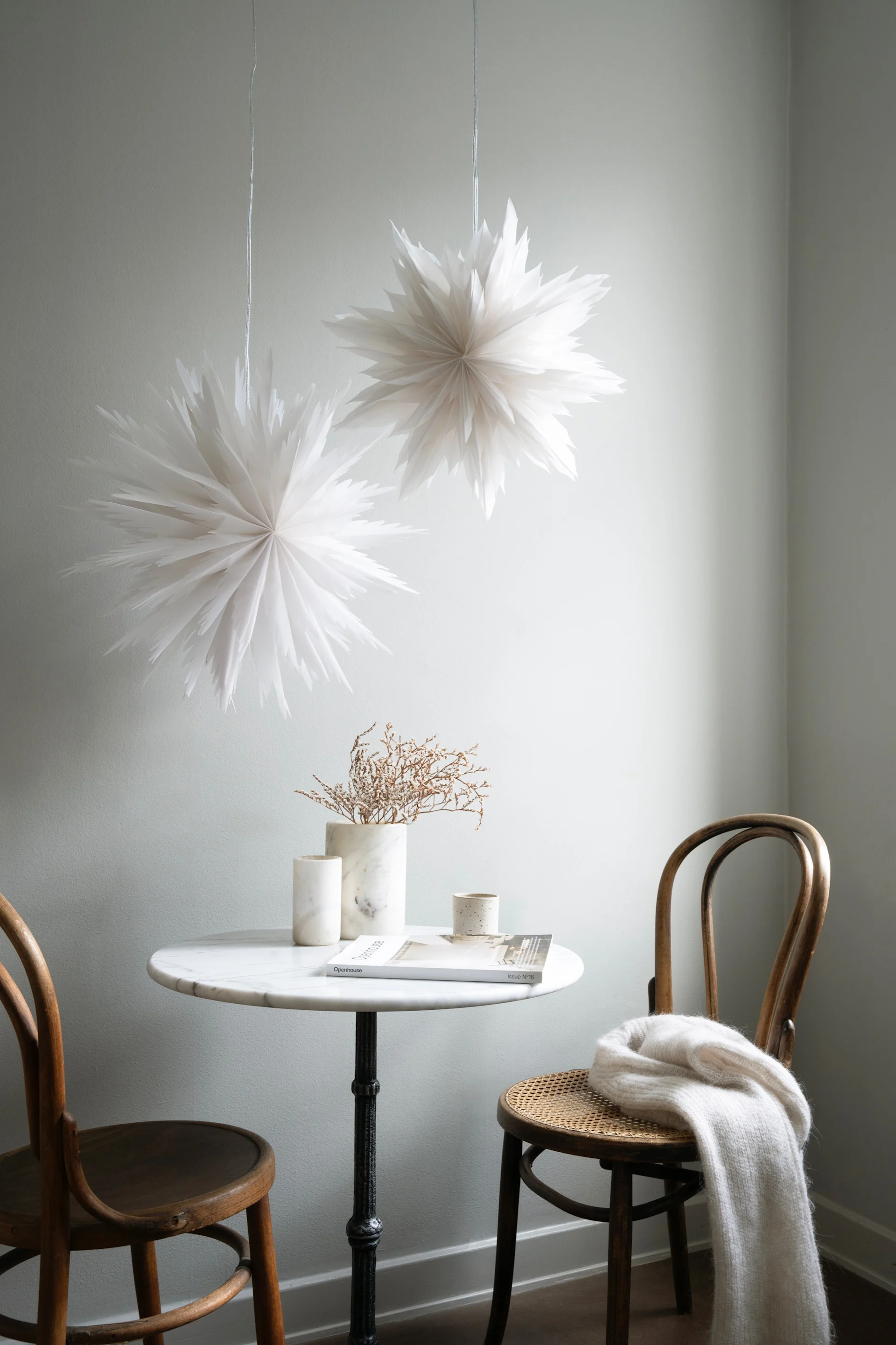 Two white Advent stars from Watt & Veke hang above a small round table with two wooden chairs.