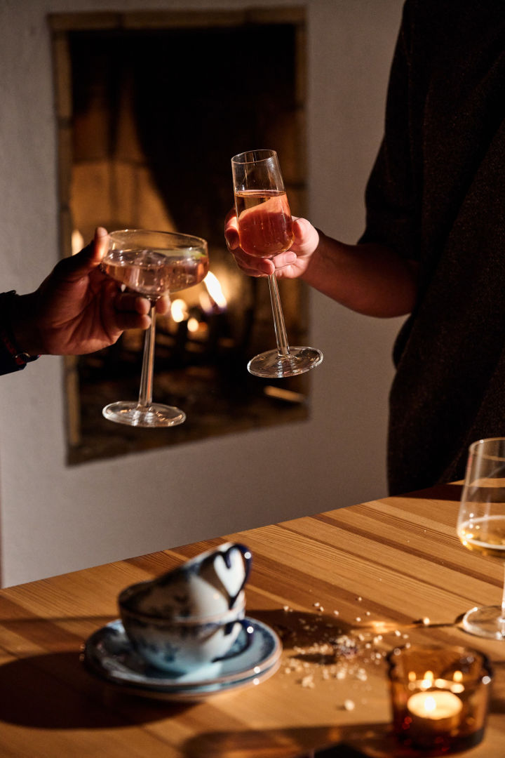 Hands hold the essence cocktail glasses and champagne glasses in front of the fire. 