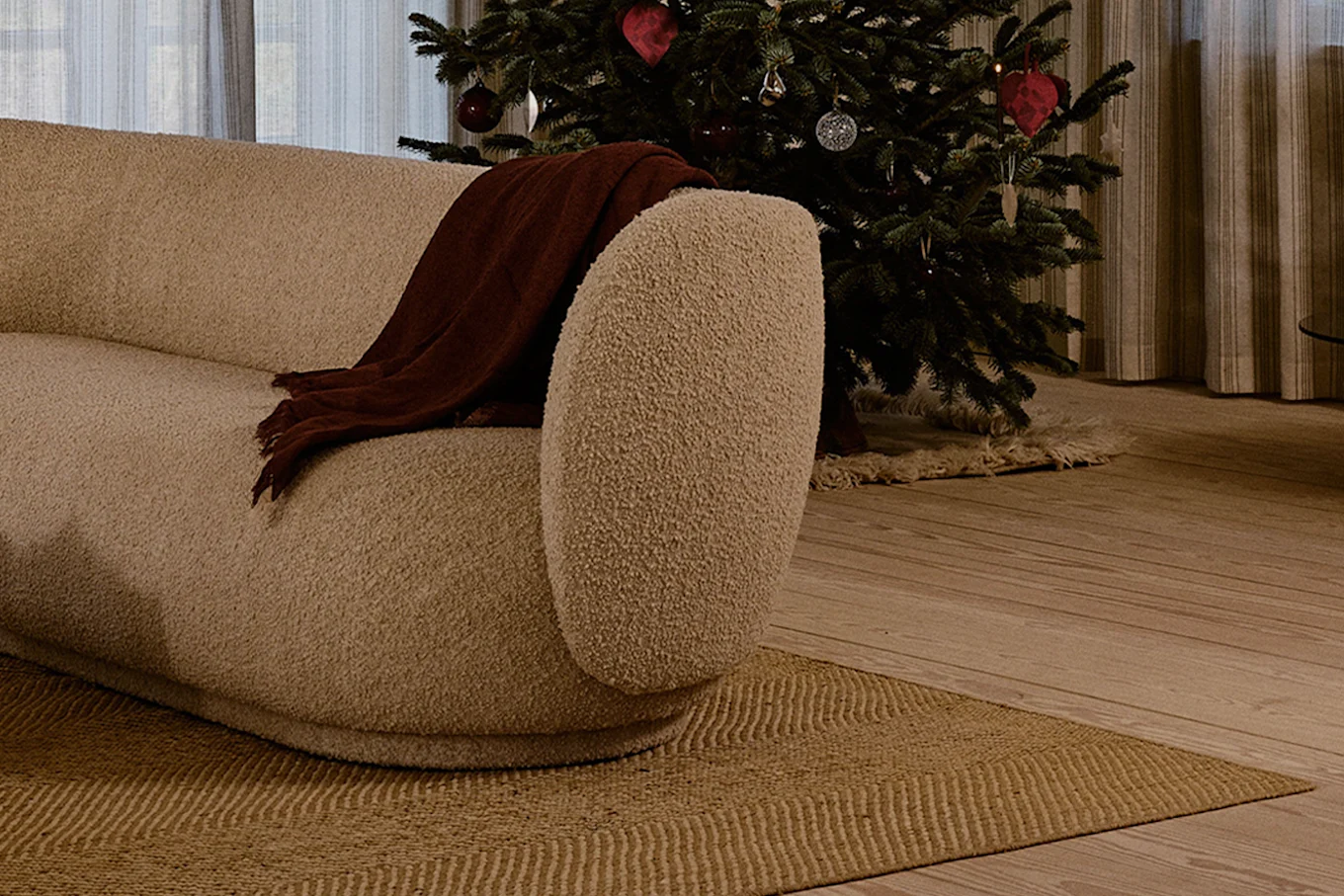 Cream curved sofa with a brown throw blanket, next to a decorated Christmas tree in a cozy living room.