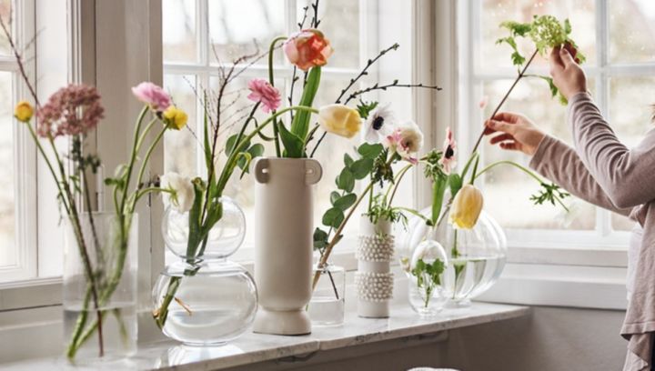 A collection of vases in clear glass with colourful spring flowers stand in a window sill. 