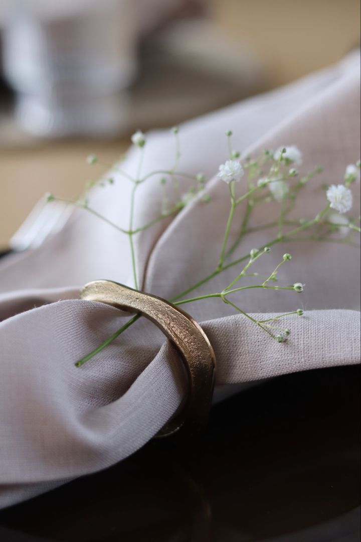 A close up of a folded napkin with a flower and a golden napkin ring. 
