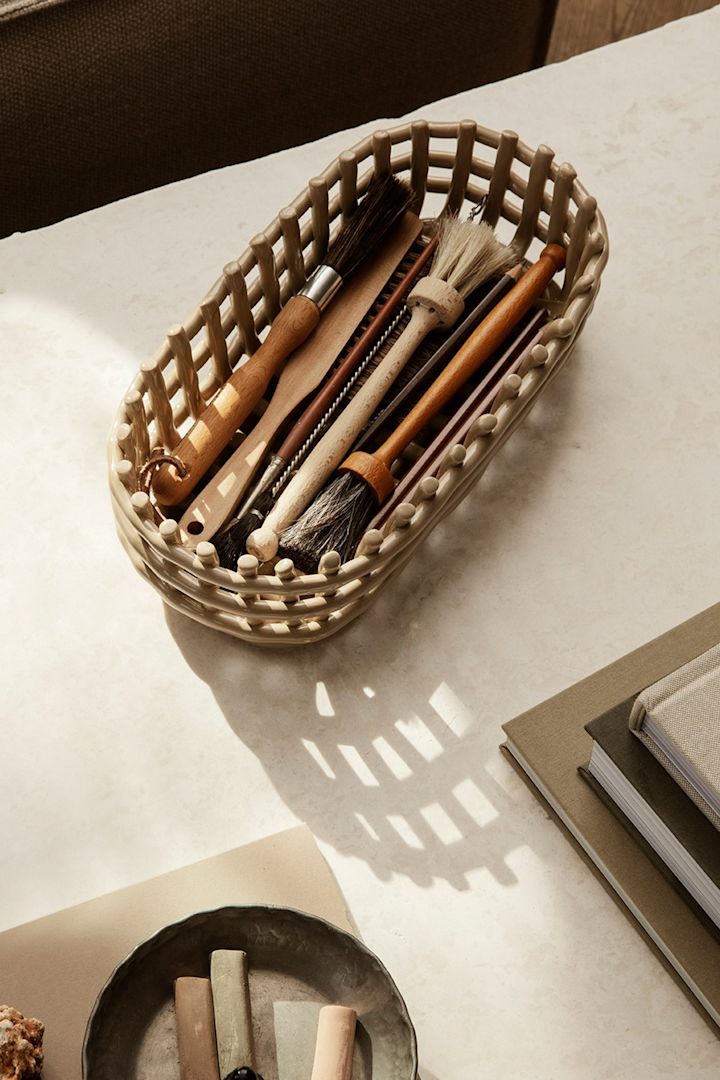 The Ferm Living ceramic basket helps you declutter your home, seen here filled with paint brushes and placed on a desk. 
