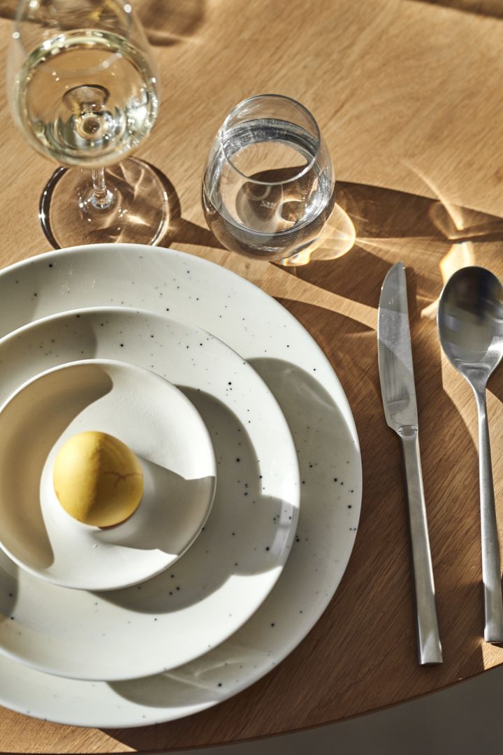 Here you see a stack of white freckle plates with a yellow egg for a simple and elegant Easter table setting idea. 