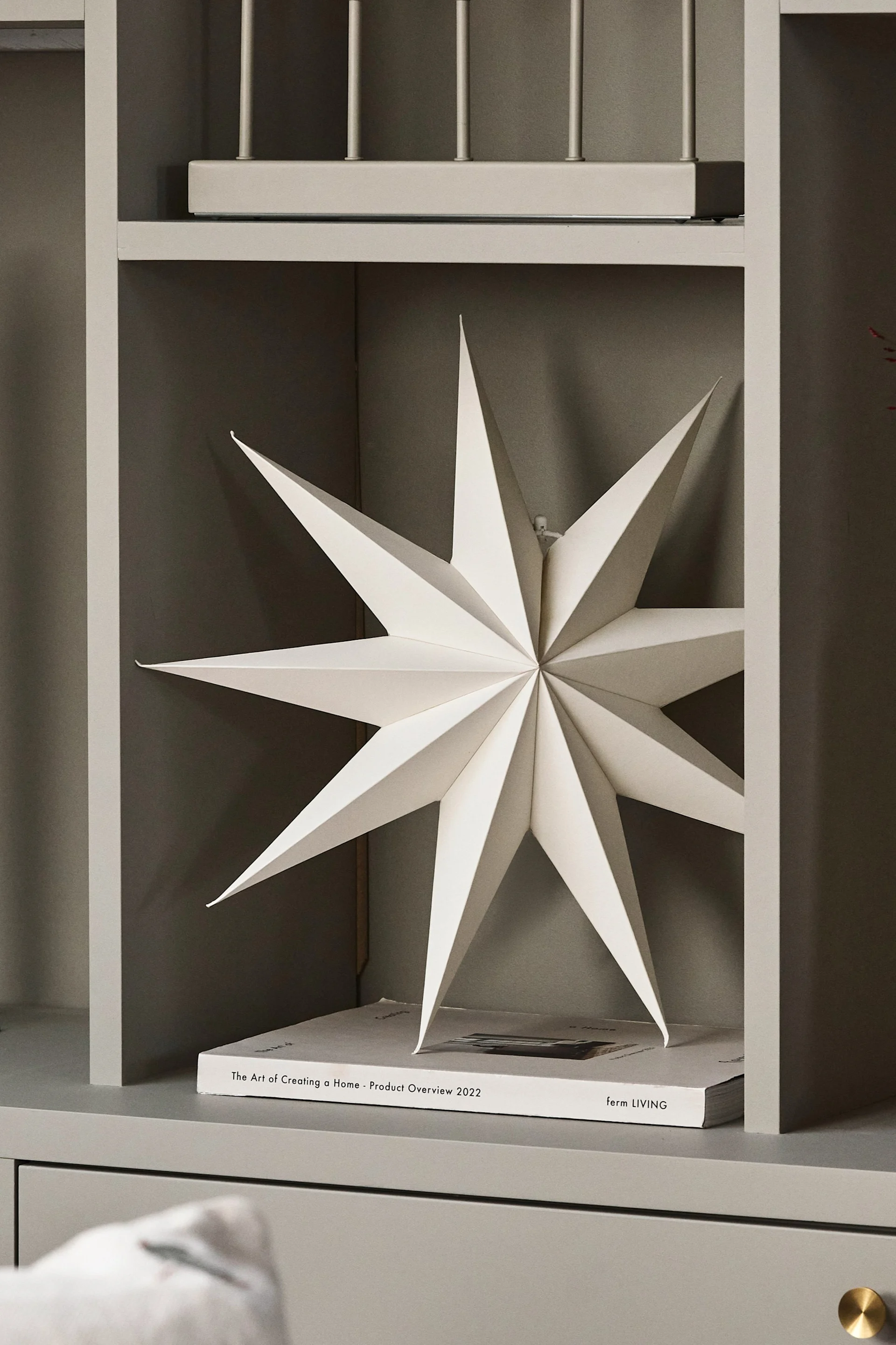 The paper star lantern for Christmas - Venja - from Broste Copenhagen hangs in the window with a pair of candlesticks and a vase.