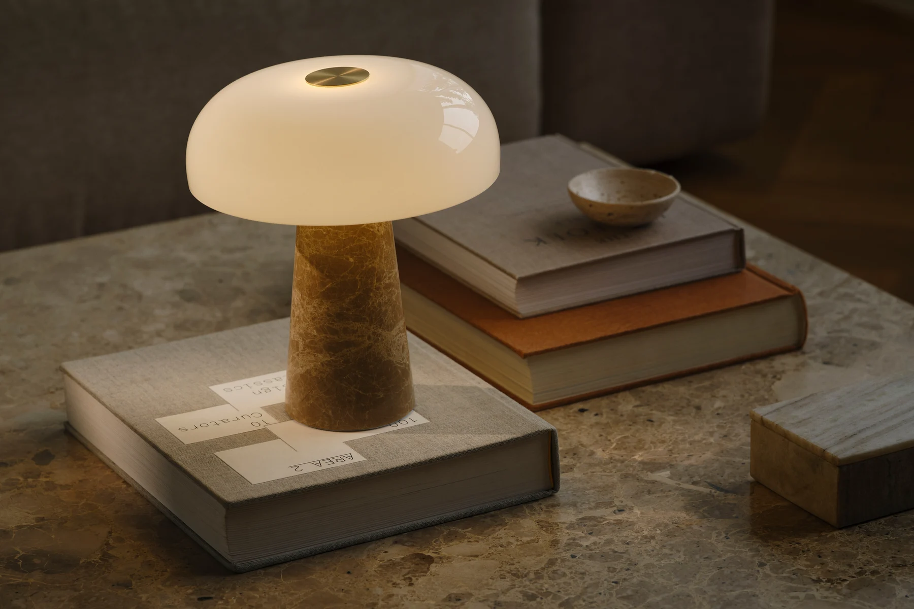 A mushroom-shaped table lamp with a white glass shade and a conical marble base sits on a marble table with stacked books.