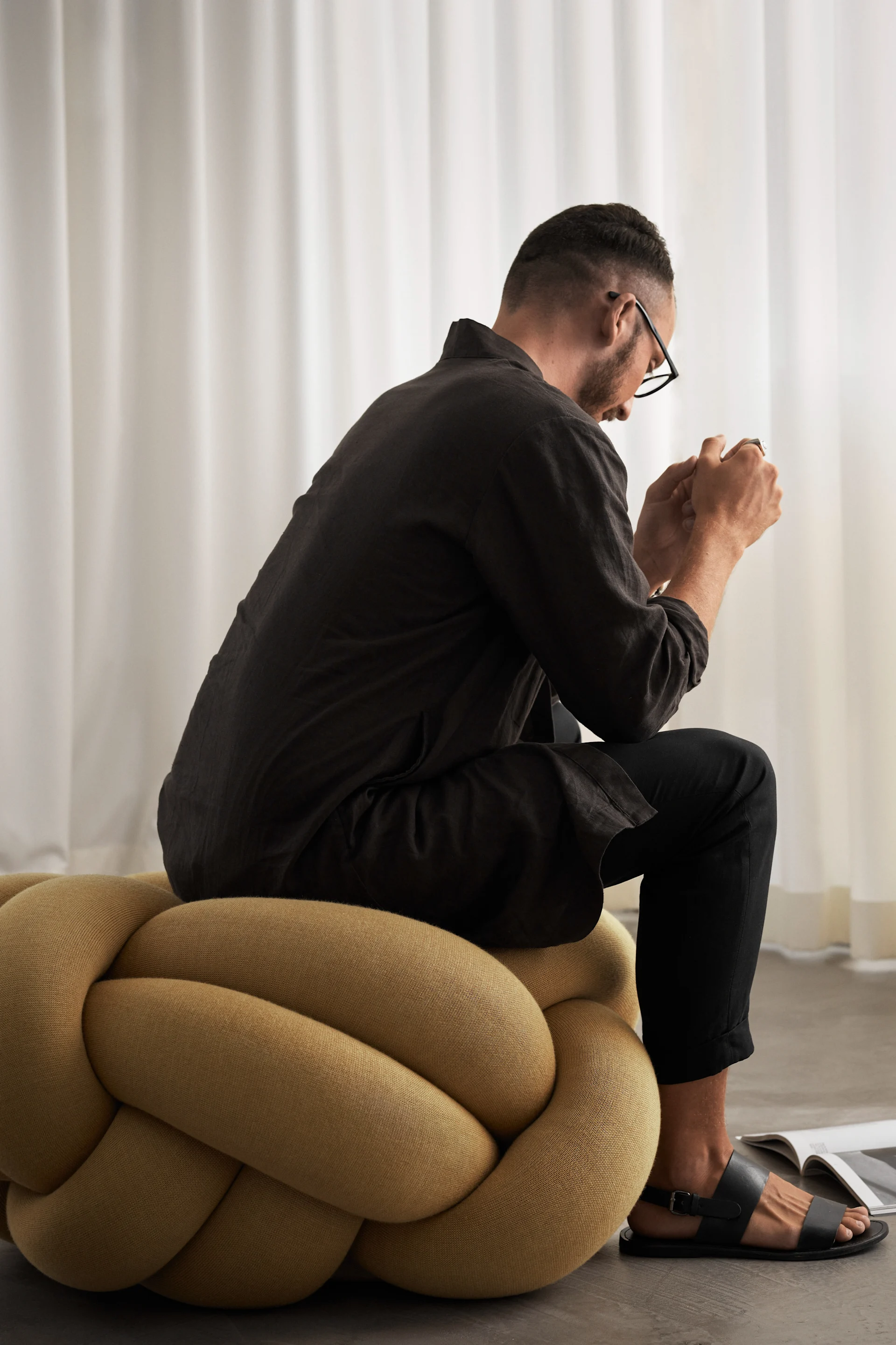 Man sits on the XL Knot Cushion in yellow. 