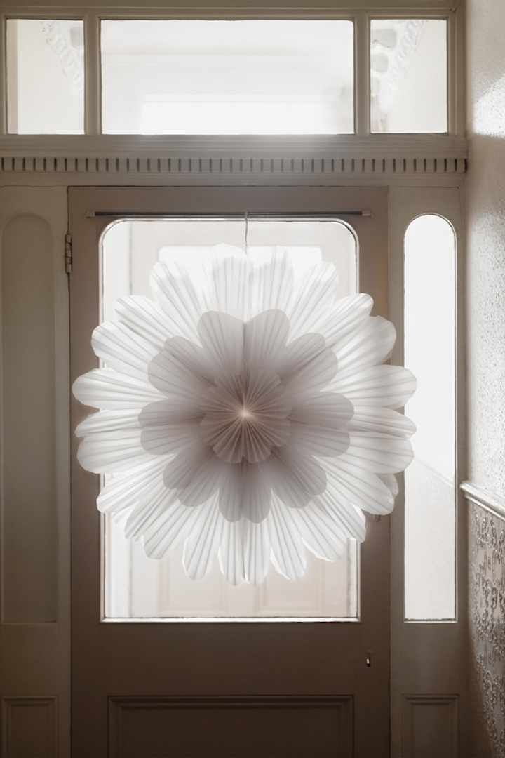 The snöblomma paper star from Watt & Veke hangs in a hallway on a front door with the light shining from behind. 