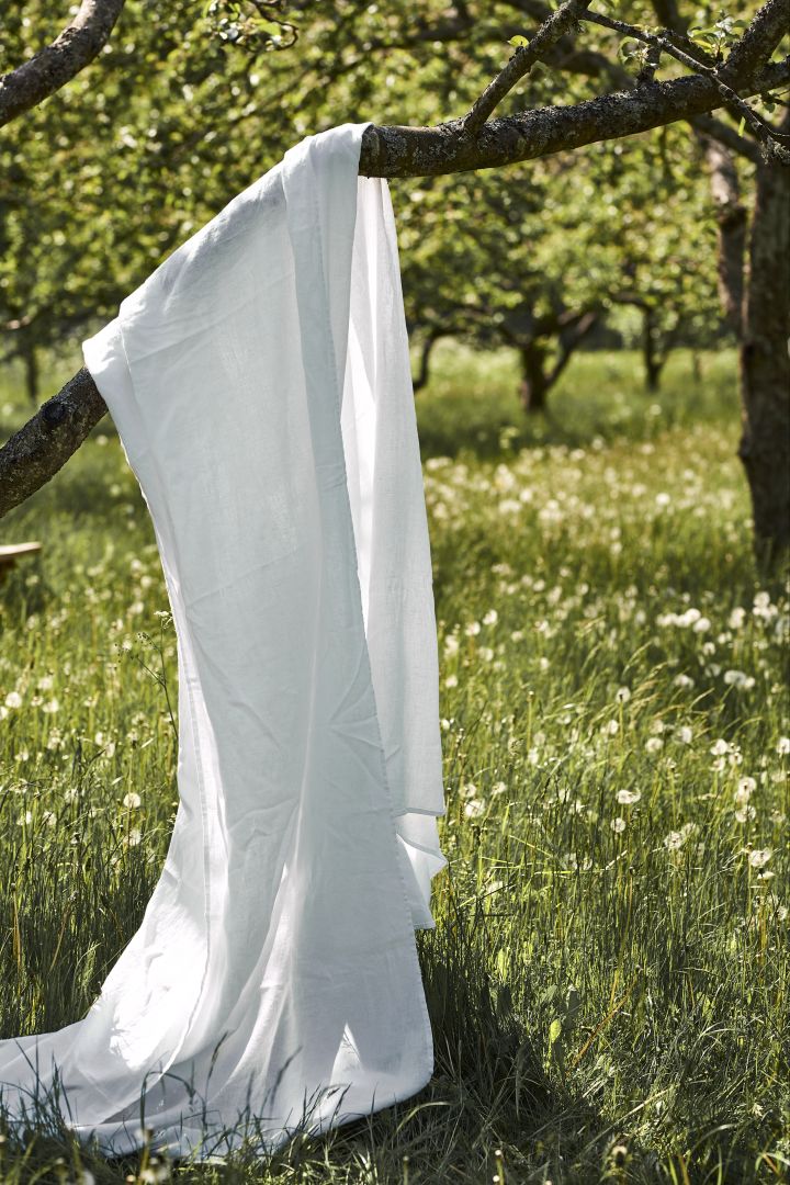 Discover our garden party inspiration with a white linen tablecloth from Scandi Living, seen here hanging in a tree in the garden. 