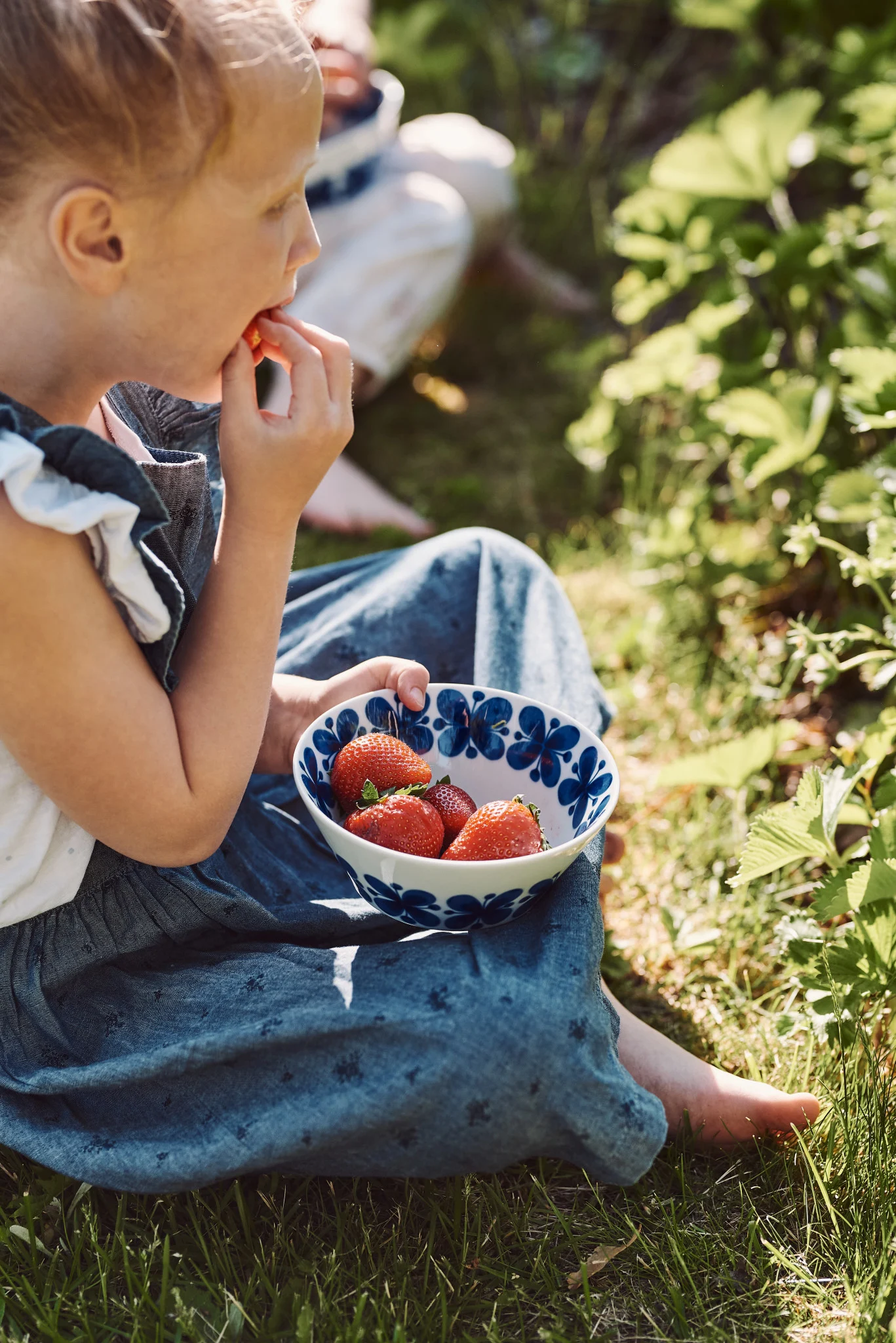 Discover simple summer recipes, here you see a young girl picking and eating strawberries from a blue and white bowl. 