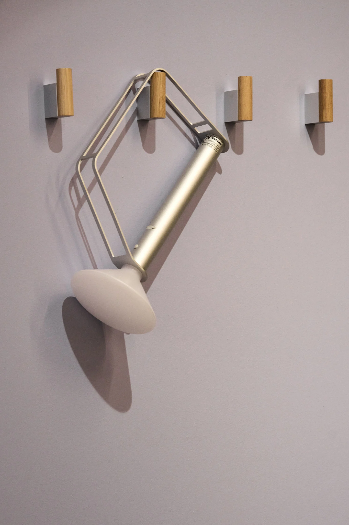 The silver, portable Piton table lamp from Muuto hangs on one of four hooks on the wall.