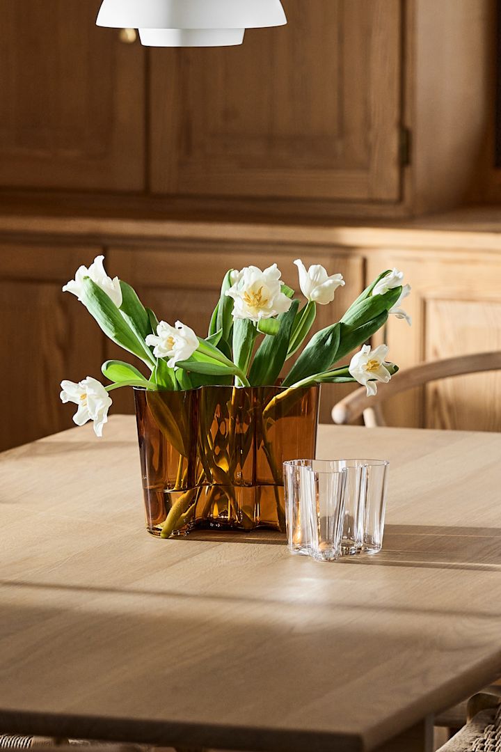 The copper colour Aalto vase on a wooden dining table with white tulips. 