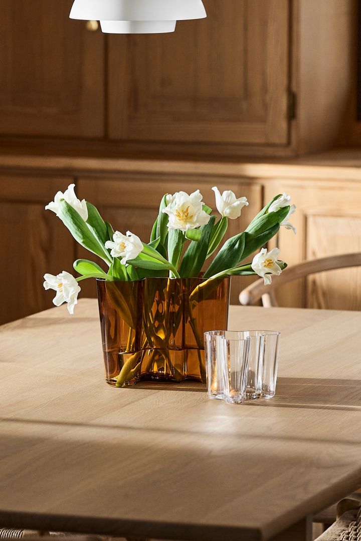 The copper colour Aalto vase on a wooden dining table with white tulips. 