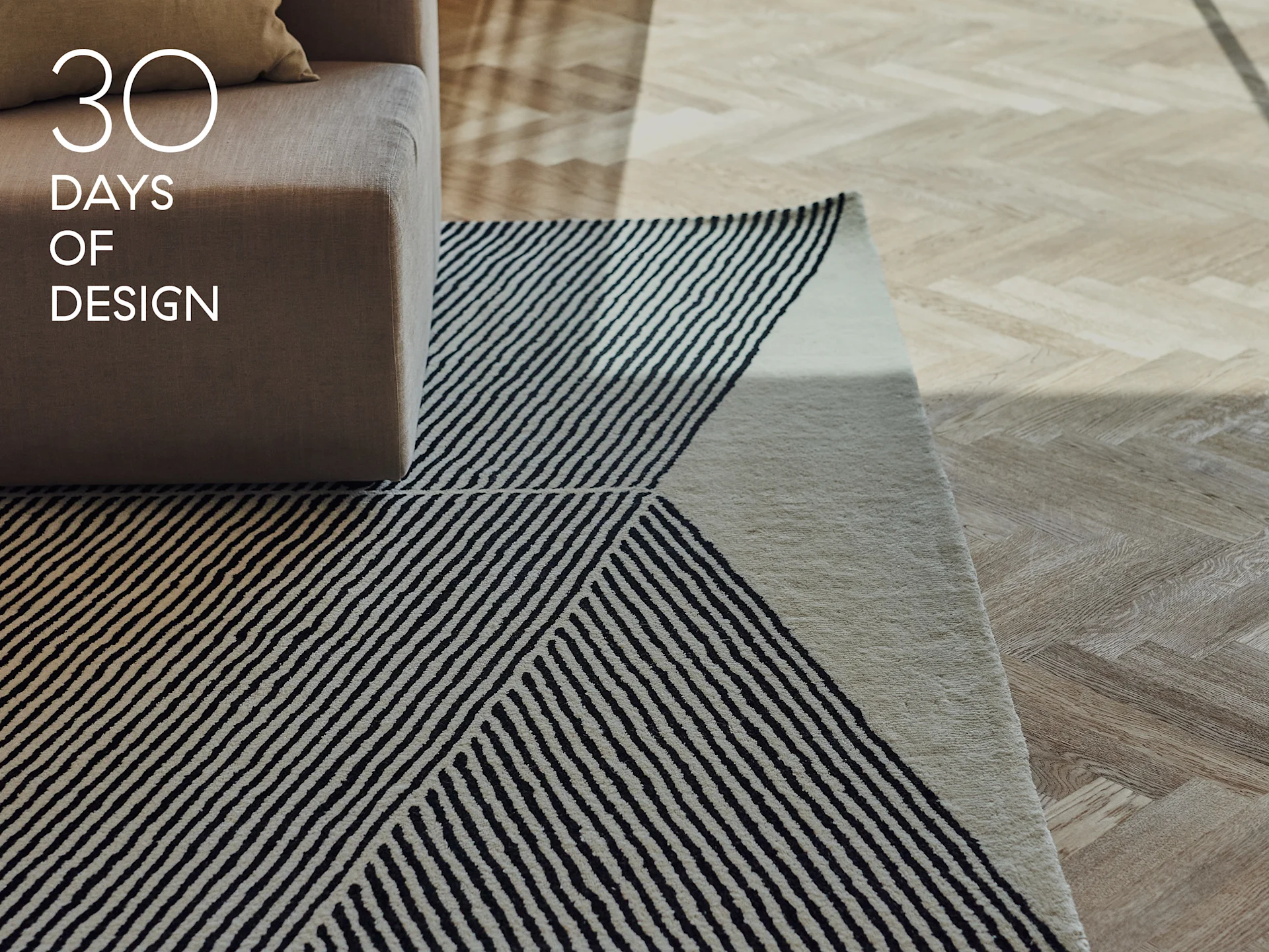 Sofa armrest, rug with geometric black and white stripes, and light wood herringbone floor. Text: 30 DAYS OF DESIGN.