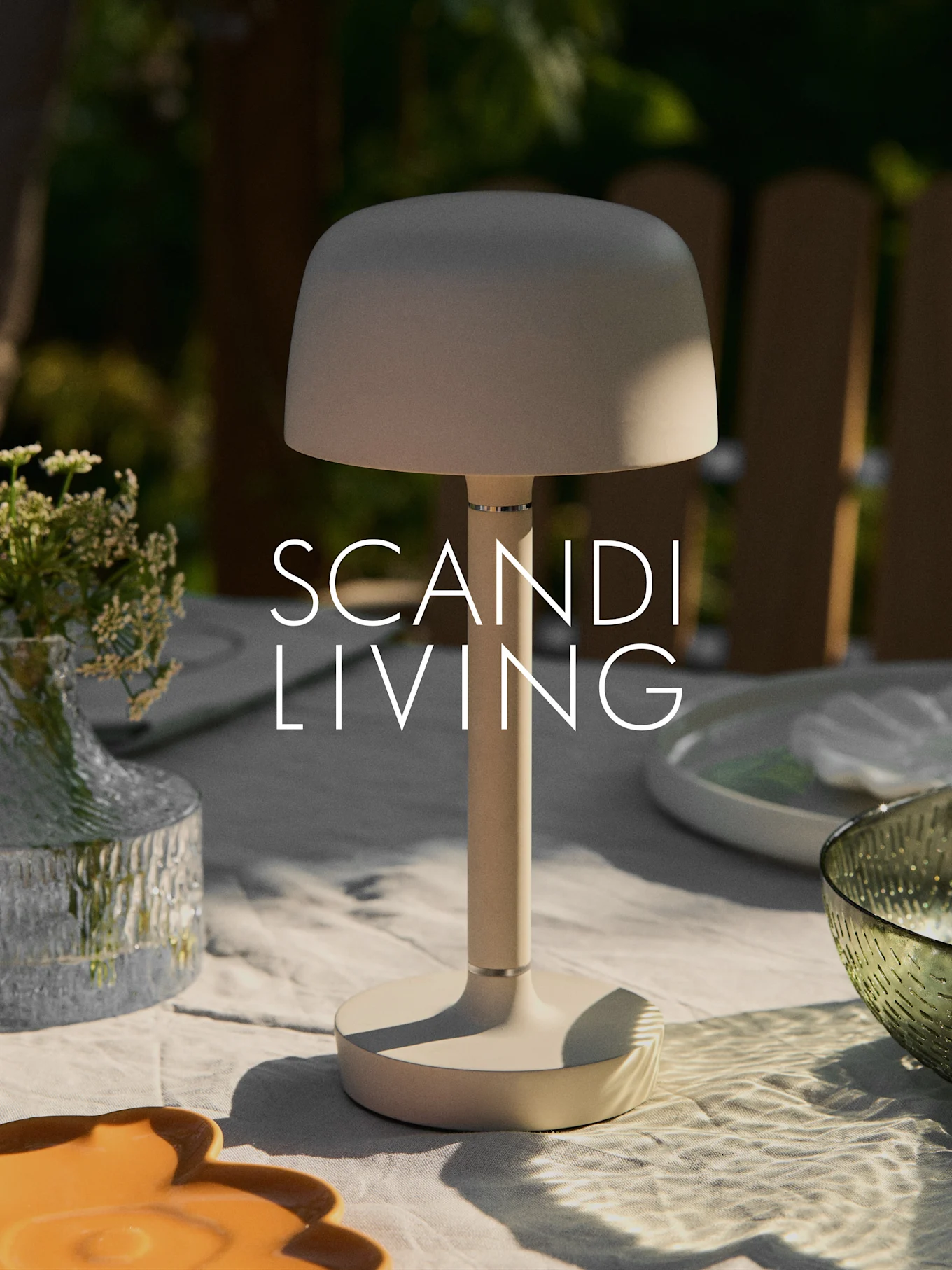 A beige modern portable table lamp on an outdoor table with a vase of flowers and dishes. "SCANDI LIVING" text.