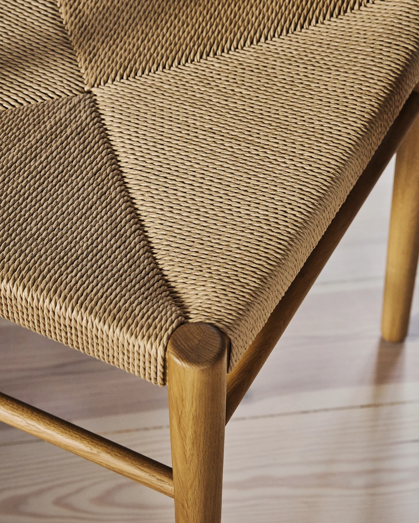 Close-up of a chair seat with natural fiber woven in a diagonal pattern, showing the wooden frame.