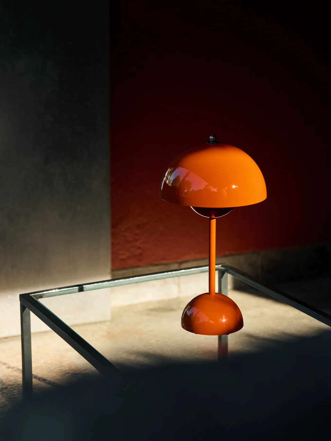 Orange mushroom-shaped table lamp on a glass table, reflecting greenery.