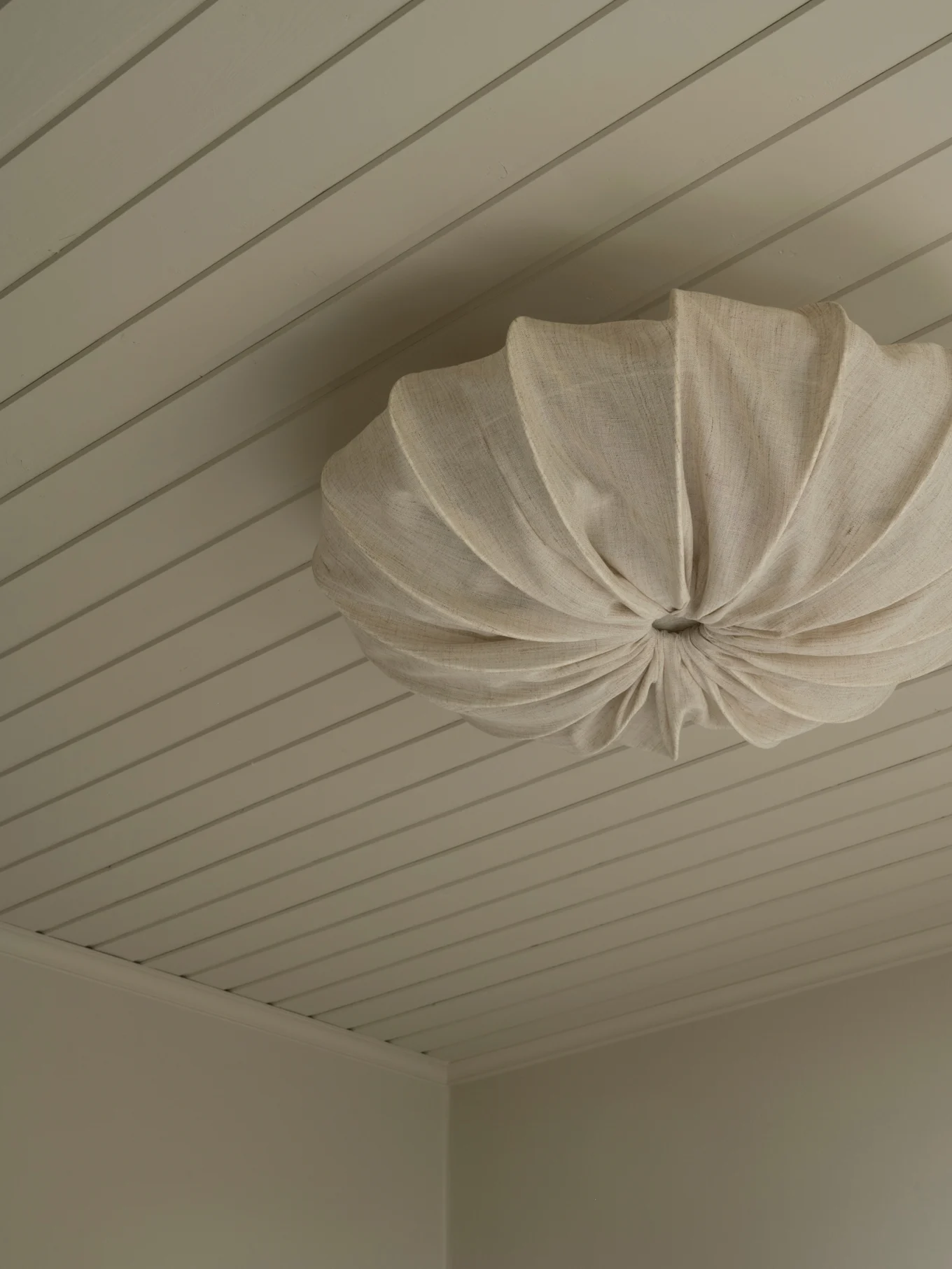A cream pleated fabric ceiling light fixture mounted on a light paneled ceiling.