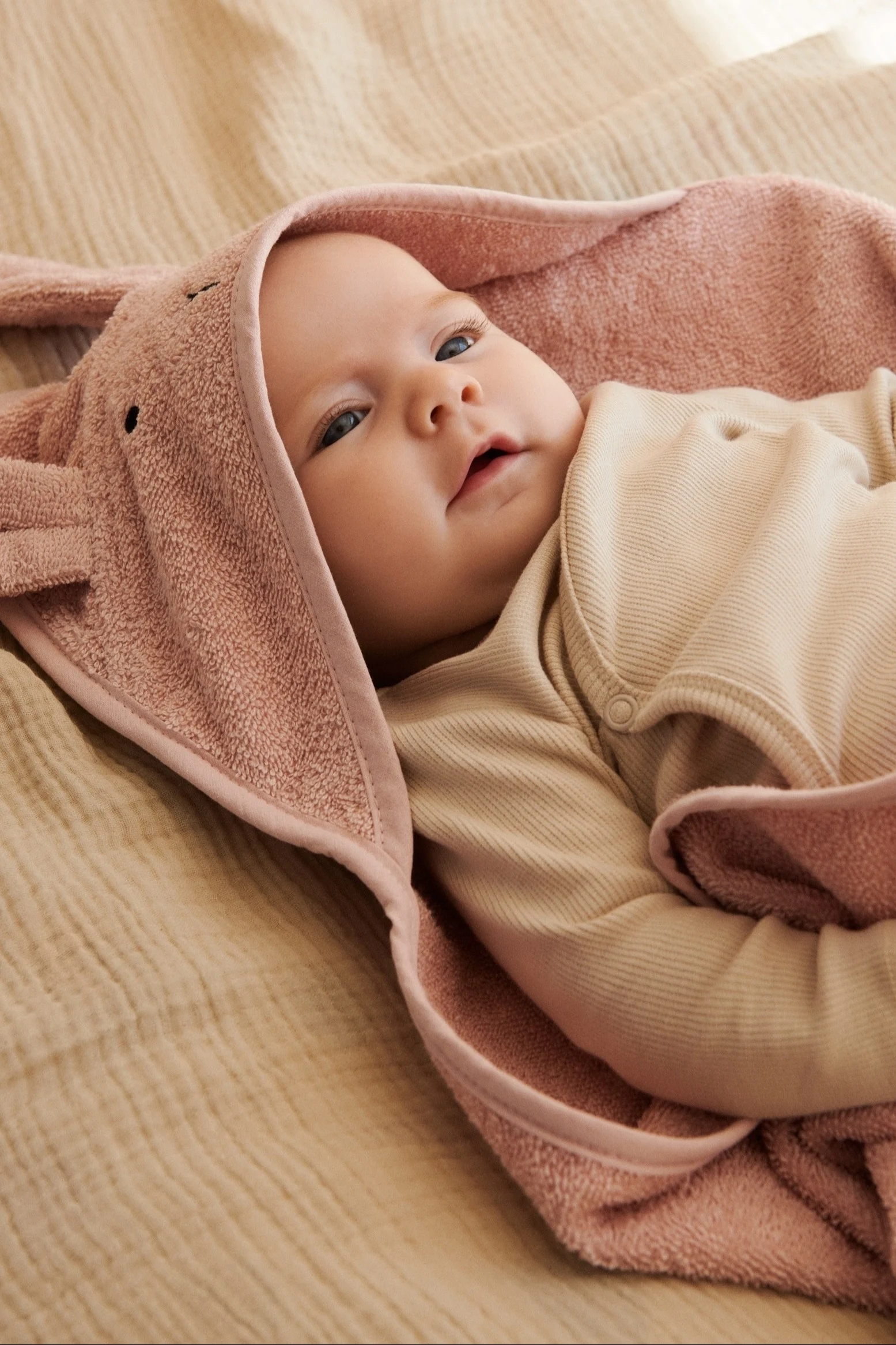 A baby lays on a towel with a hood in a matching baby grow from Garbo&Friends - perfect baby shower gift ideas. 