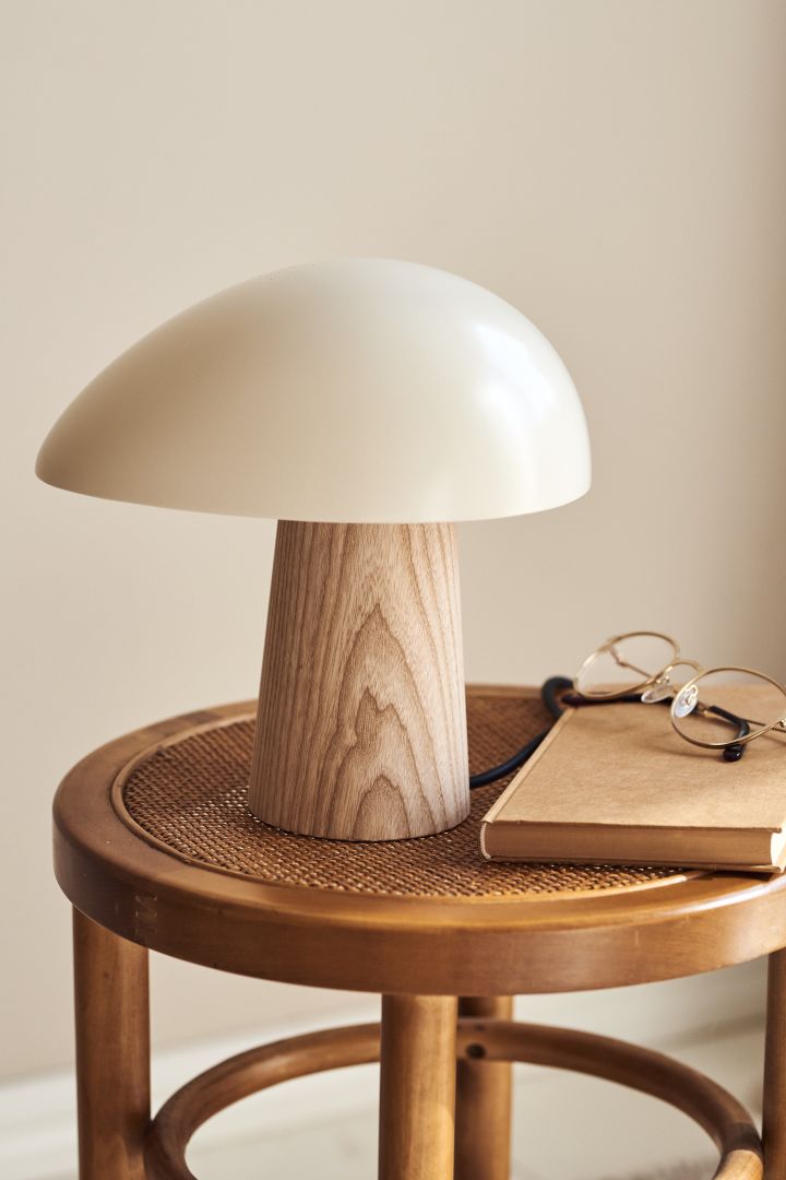 Renew your home with modern table lighting - here you see Fritz Hansen Night Owl table lamp in white and light wood on a stool of rattan.