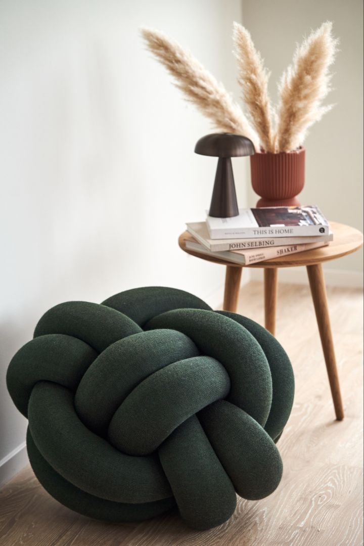 The Knot cushion in forest green with the Como portable lamp from &Tradition and a vase filled with pampas grass. 