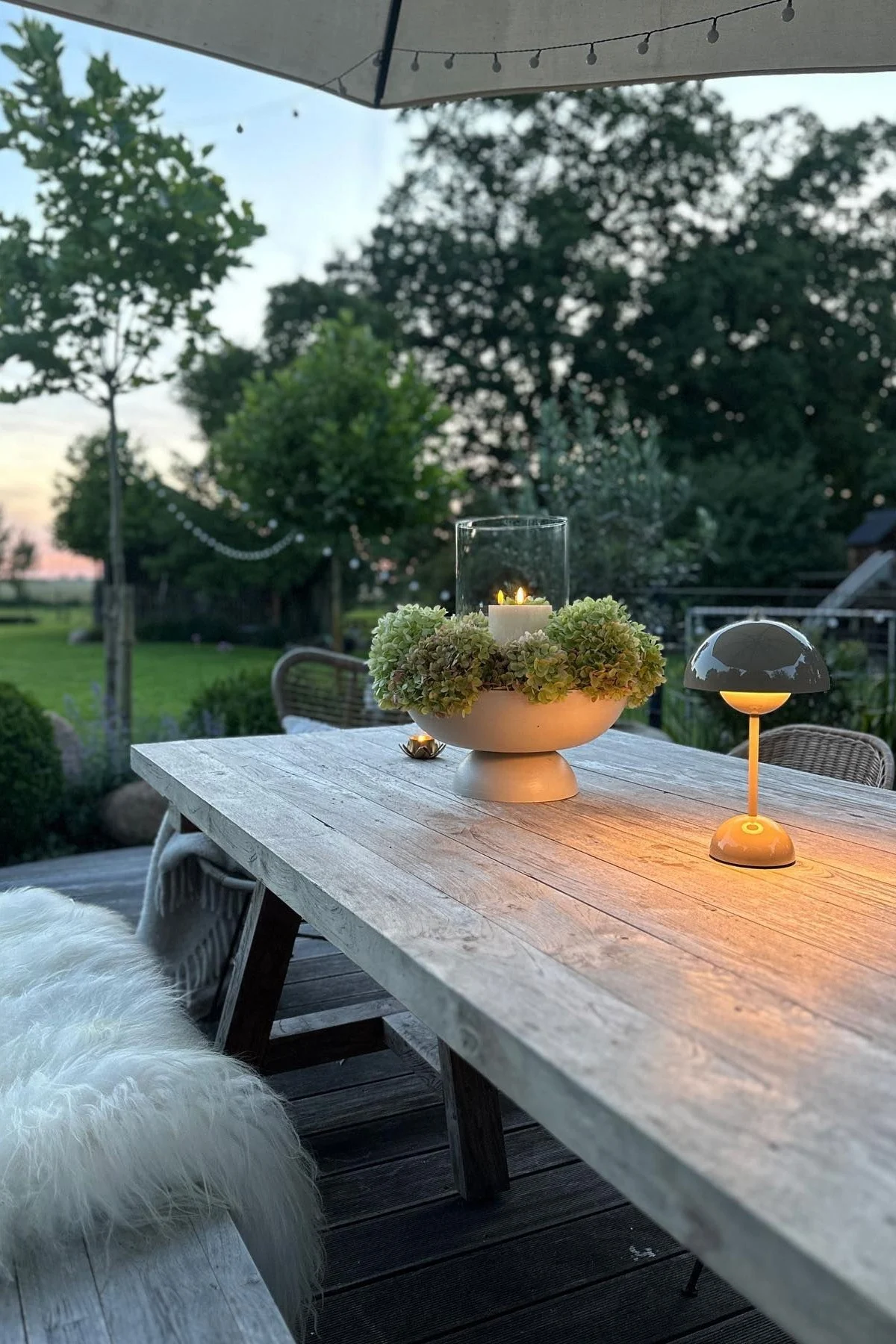 A cosy terrace with a large dining table and benches, decorated with candles and a Flowerpot table lamp from &Tradition.
