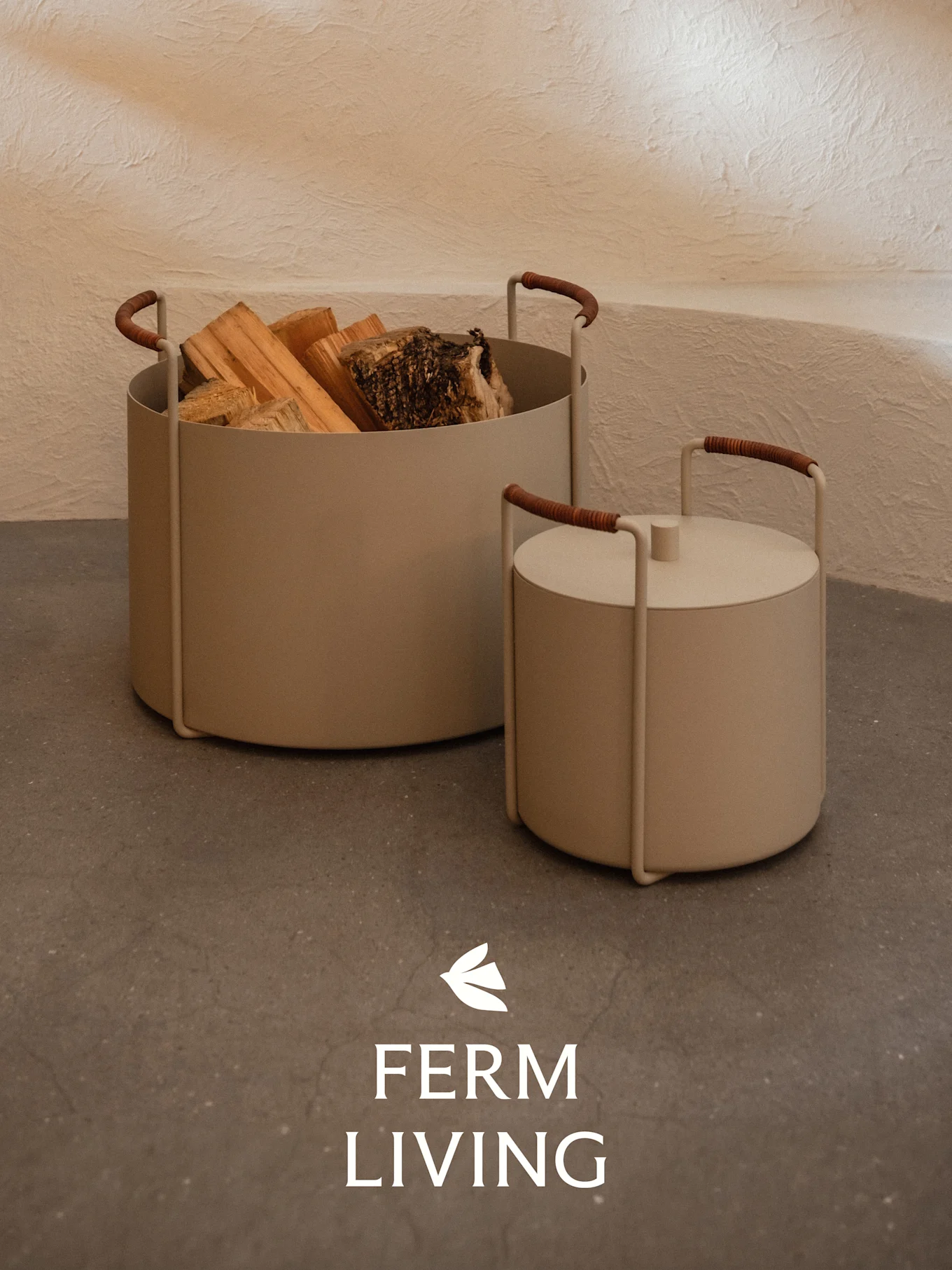 Two beige cylindrical containers, one holding firewood and the other lidded, with brown-wrapped handles on a concrete floor.
