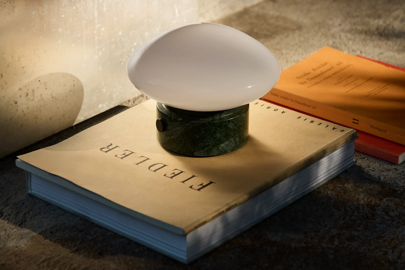 A dark blue mushroom-shaped table lamp with a silver stem and base sits on a reflective table next to a stack of books.