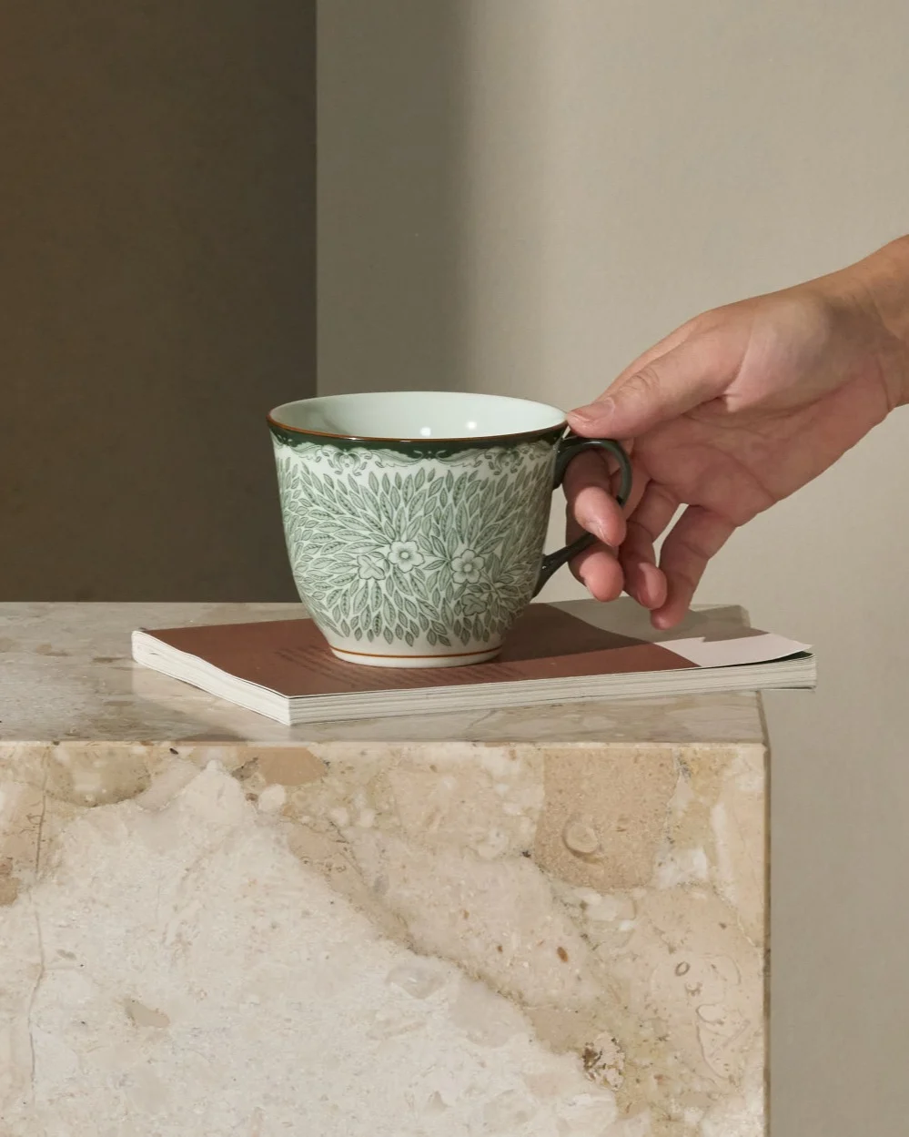 Person reaching for a green patterned cup on a marble side table next to a sofa.
