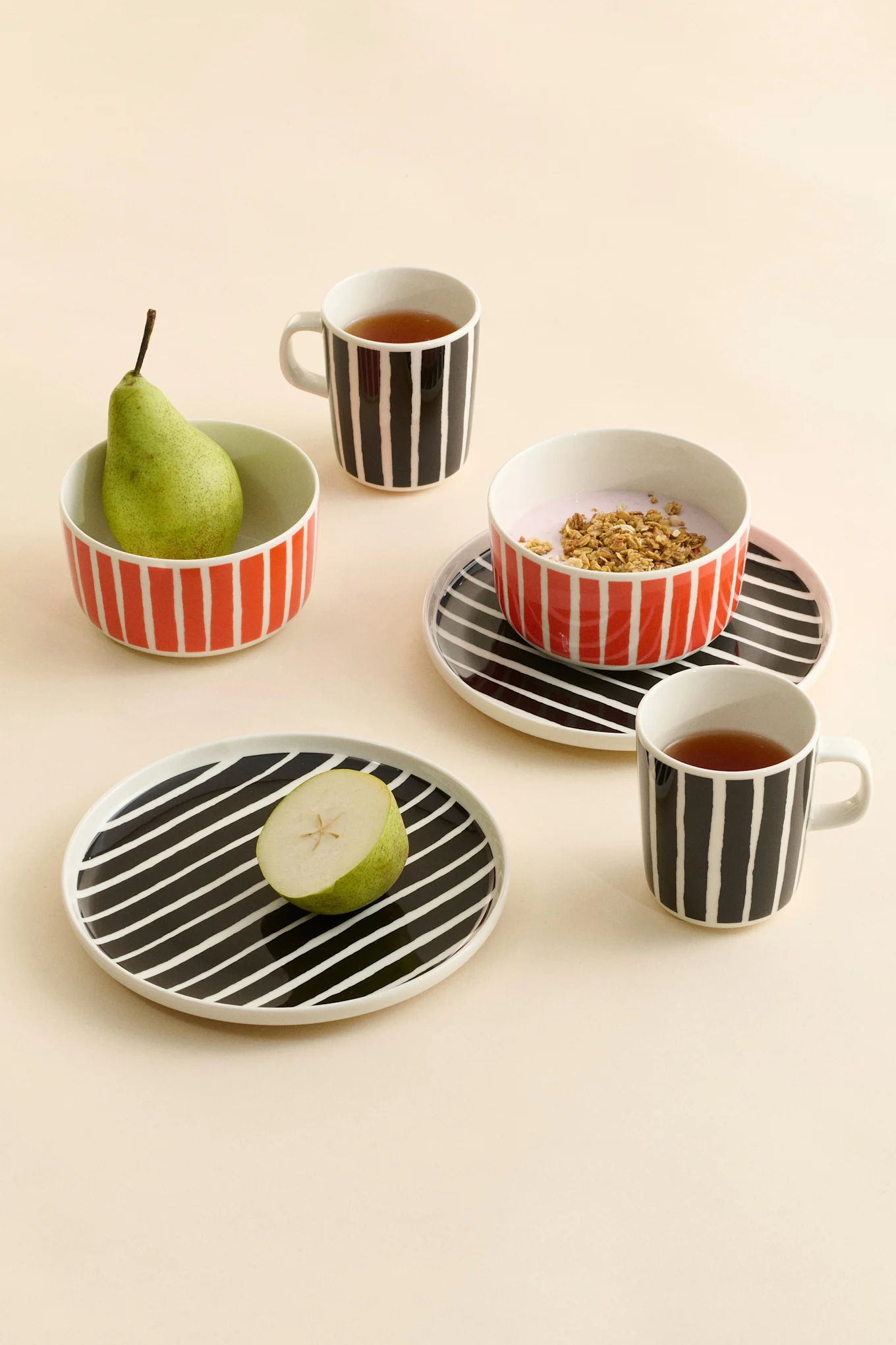 Striped ceramic mugs with tea, bowls with a pear and yogurt with granola, and plates with a half pear.