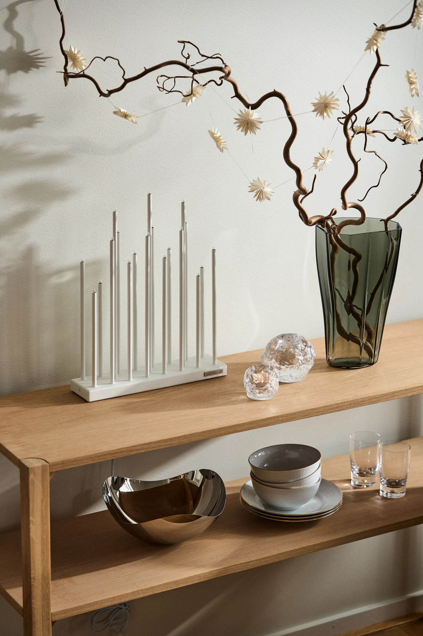 The Elflugan Advent candle holder on a wooden sideboard together with the snowball candle holder from Kosta Boda and a vase filled with branches. 