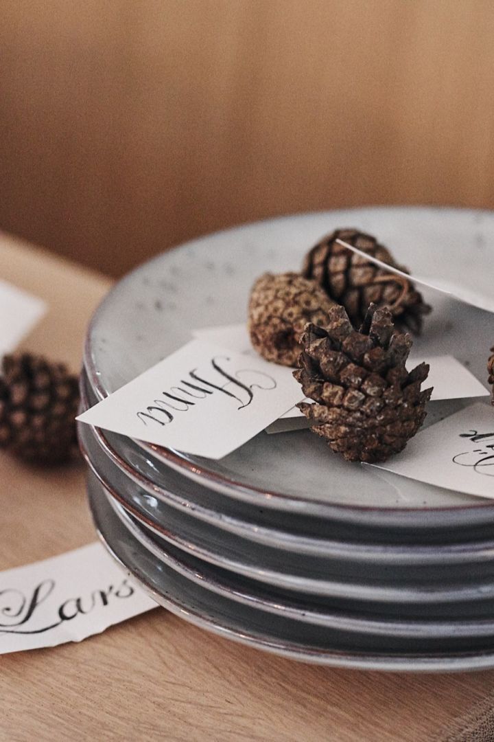 Pine cones as place card holders rest on a stack of stoneware plates from Broste Copenhagen.