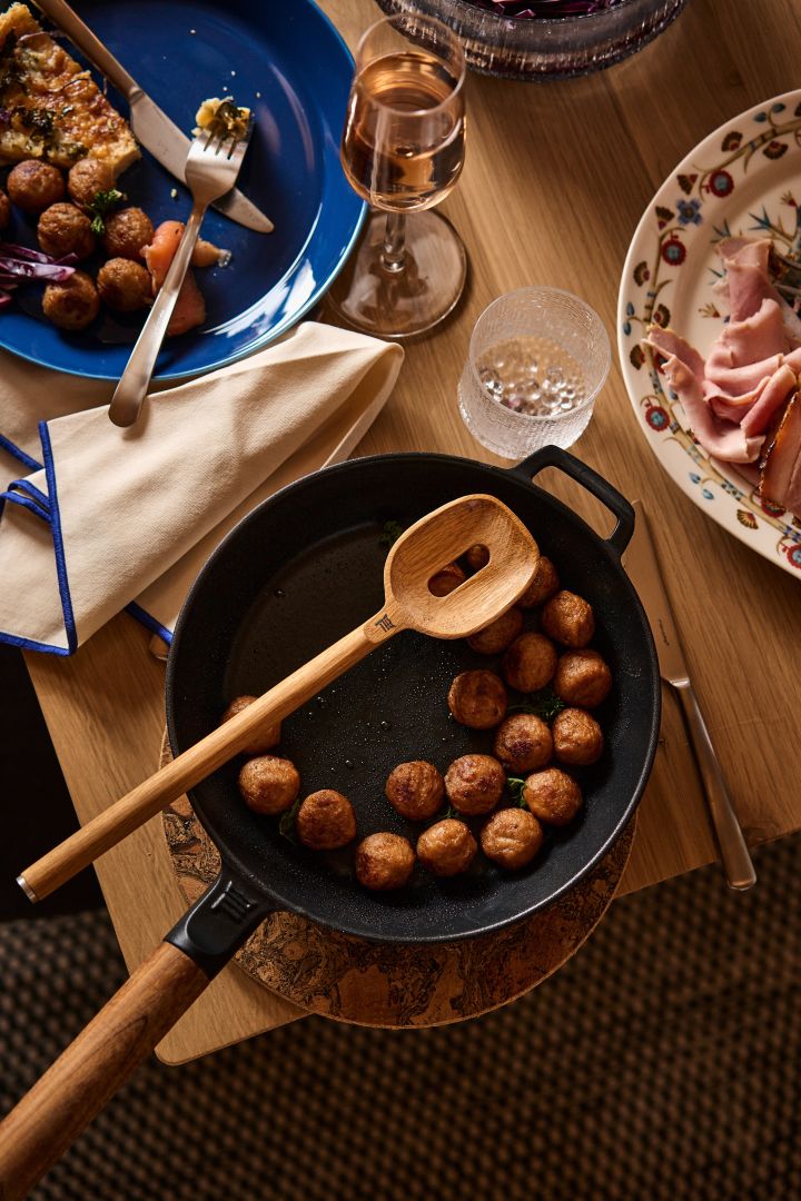 The Norden cast iron frying pan from Fiskars on a table with meatballs and wooden serving spoon, the ideal Christmas gift idea for food lovers. 