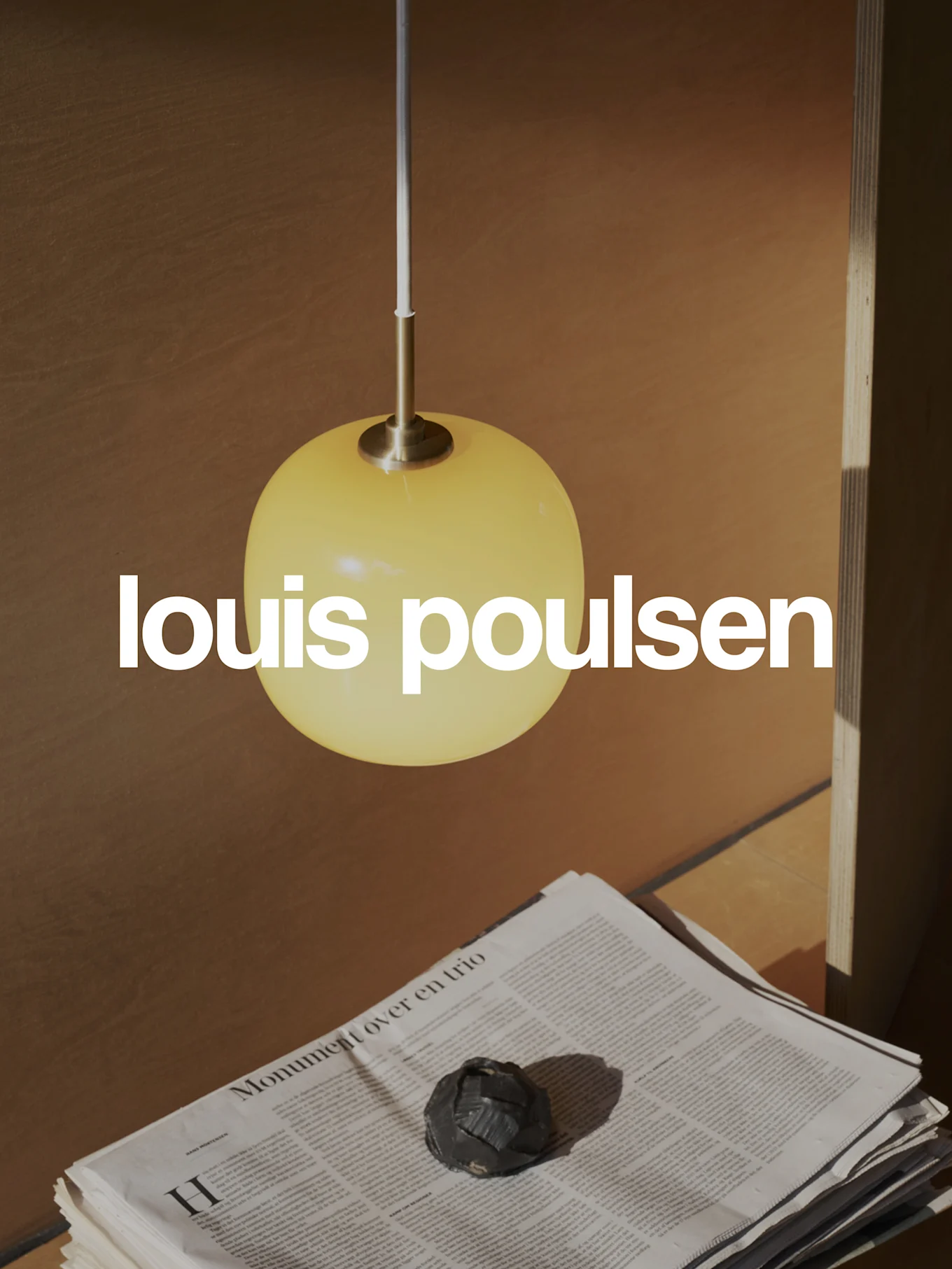 Louis Poulsen logo overlaid on a warm scene with a yellow spherical pendant lamp, stacked newspapers, and a dark decorative object.