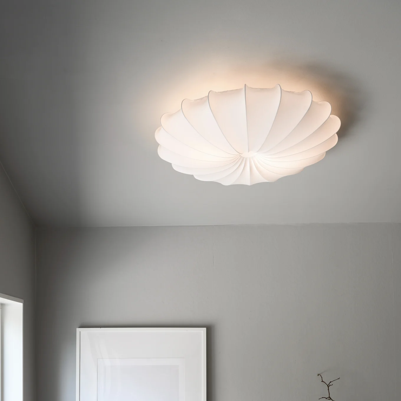 A white, pleated, shell-shaped ceiling lamp illuminates a grey ceiling.