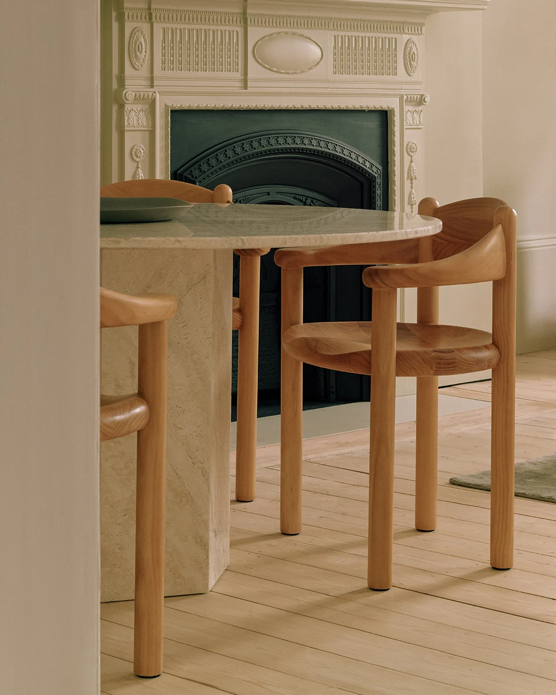 A round marble table with two light wood chairs, in front of a decorative fireplace.