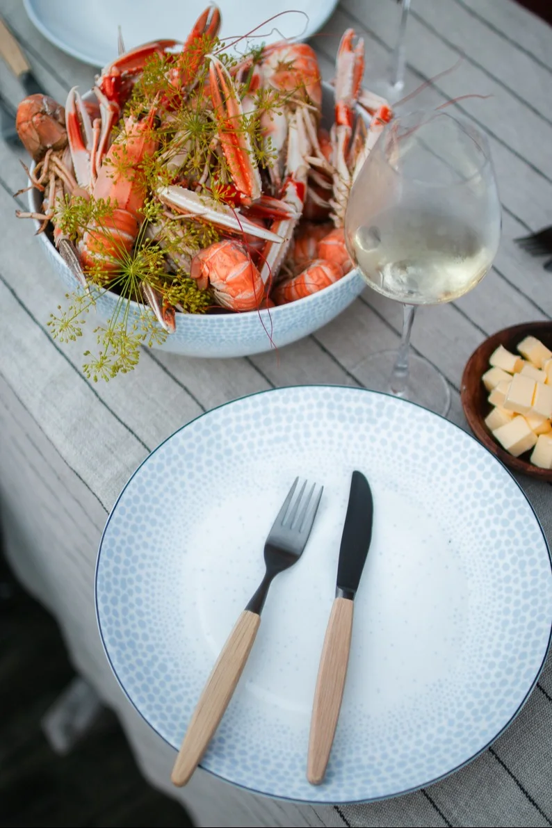 The plates from the Ocean collection by Wik&Walsoe are perfect for a Swedish crayfish party. Here, a plate with cutlery stands on a table, next to a bowl from the same collection filled with seafood.
