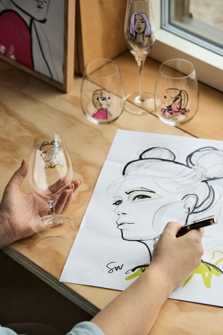 A hand holds a beer glass from the All about you collection in one hand and sketches a drawing with the other. 