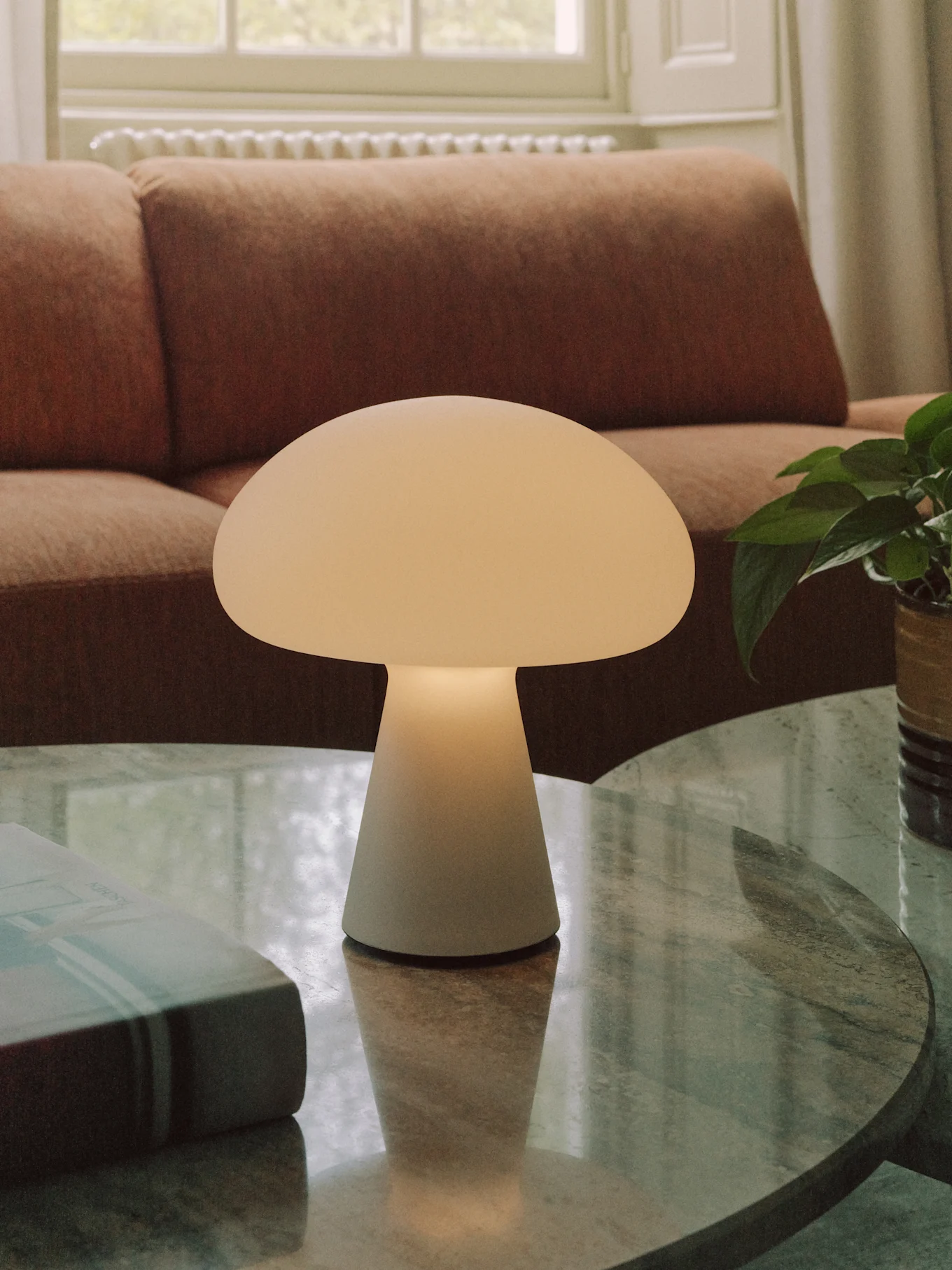 An off-white mushroom-shaped table lamp sits on a round, marble coffee table in a living room.