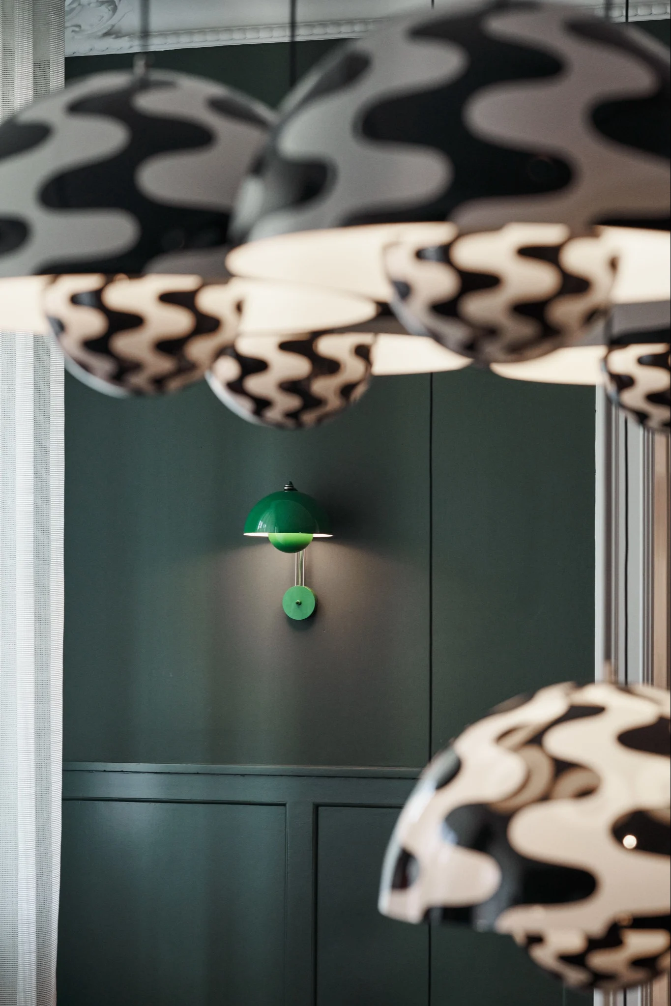 A green Flowerpot VP8 wall lamp hangs on one wall, with several black and white Flowerpot VP1 pendant lamps hanging in front of it, both from &Tradition.