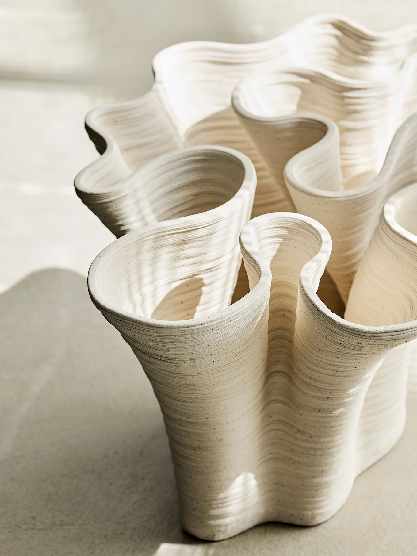 Close-up of a light beige wavy ceramic vase with rippled texture and shadow play.