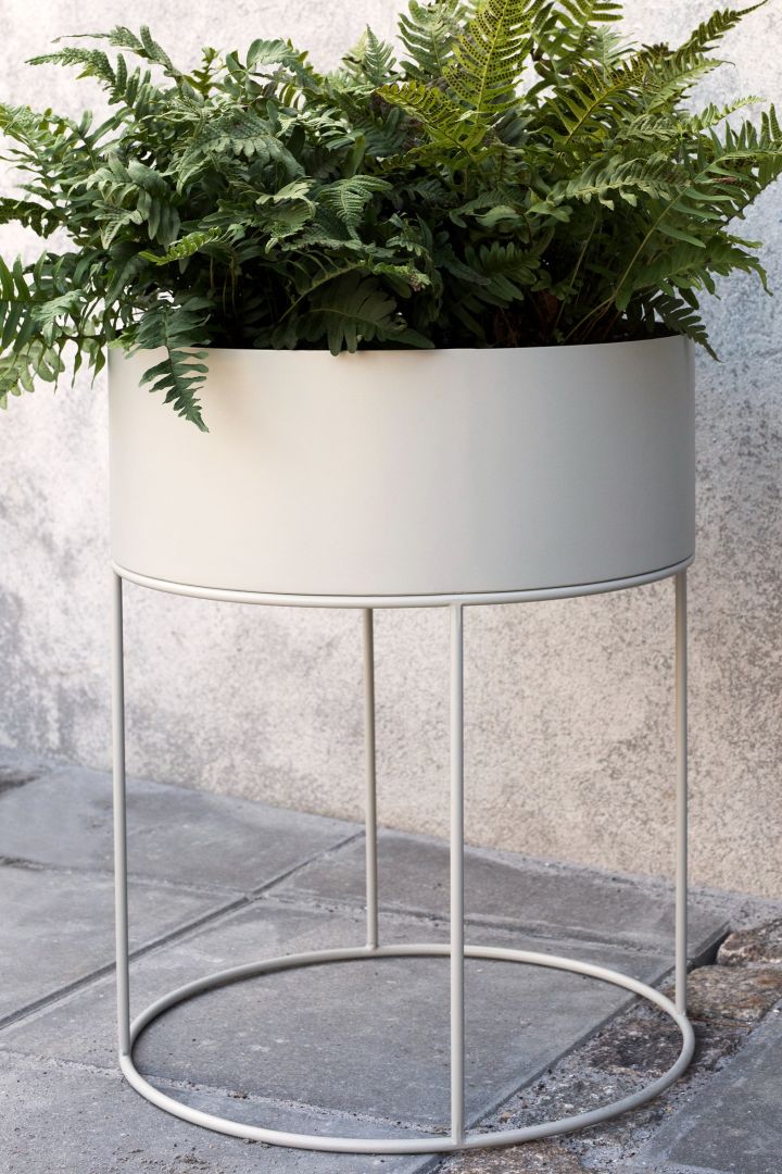 The large round metal plant box from Ferm Living with a large green fern, stands on a patio. 