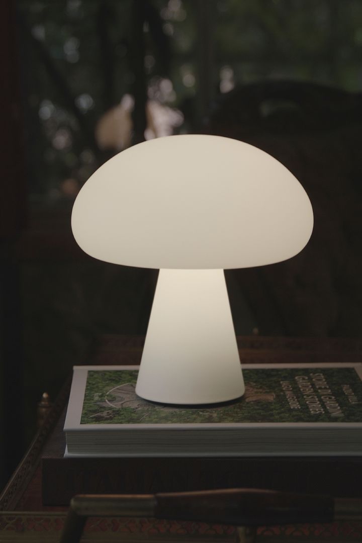The frosted glass portable mushroom table lamp from Gubi standing on a magazine outside in the dark. 