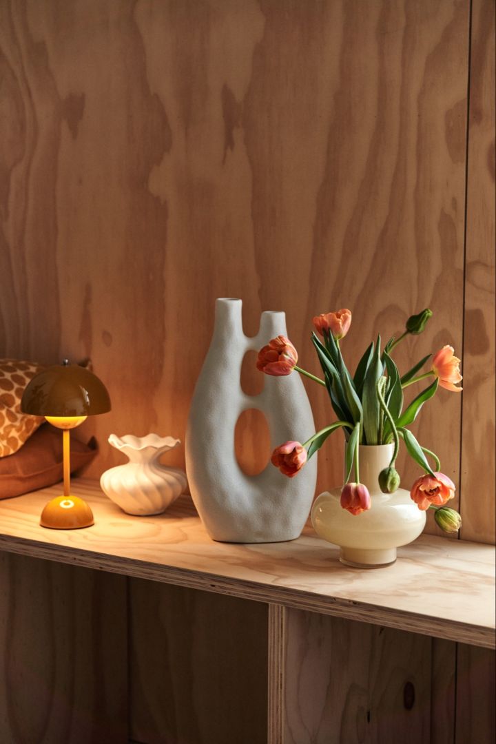 A ledge with a portable lamp, sculpture and a vase with fresh flowers to create visual interest in a room. 