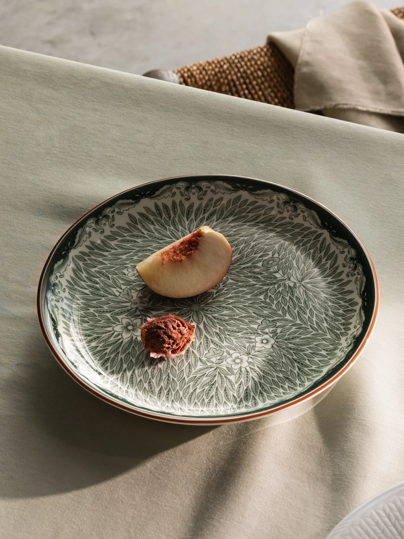 A table set with a green patterned plate holding a peach slice, and a partial view of a white plate with cream and peach slices.