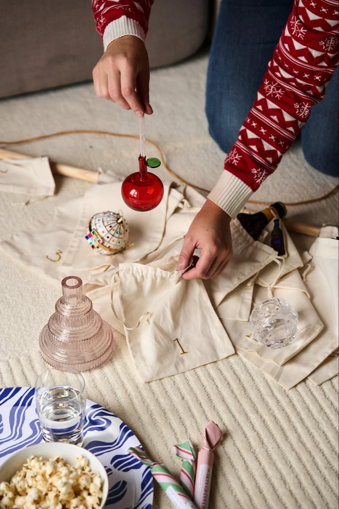 Hands place a glass red apple decoration from Iittala into the bag of an Advent calendar from ferm LIVING.